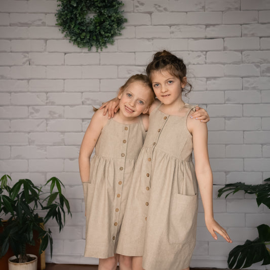 two girls wearing a handmade undyed linen sundress with pockets buttons and adjustable tie-up straps.