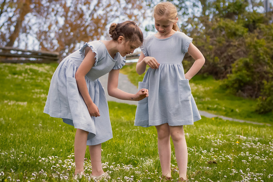 girls in blue gauze dresses in grassy field picking a daisy
