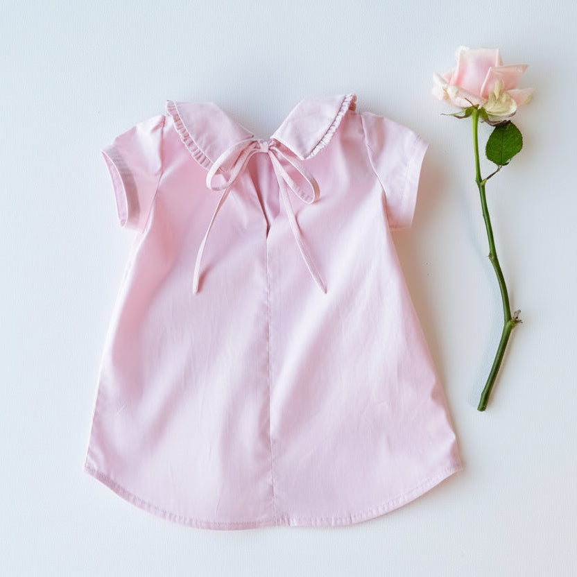 Pink blouse with a bow collar on a light blue background with a pink rose.
