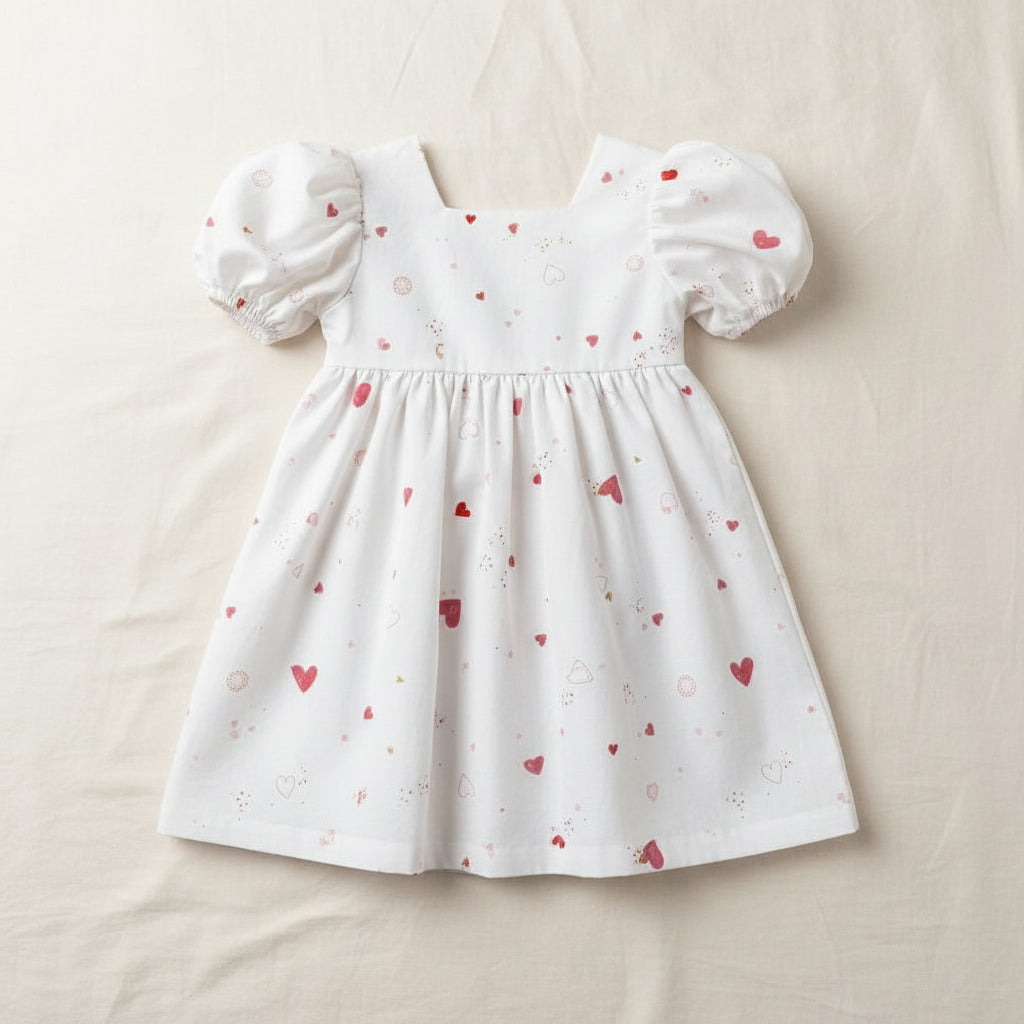 Young girl wearing a light blue dress with heart patterns against a wooden paneled wall.