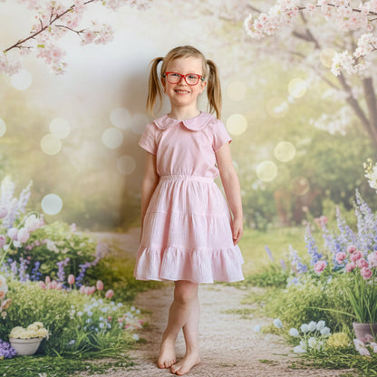 Young girl in a pink dress standing against a brick wall.
