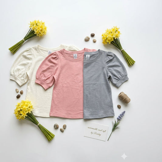 Three children's shirts in white, pink, and gray with yellow flowers and stones on a light background