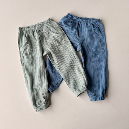 Two pairs of children's pants, one green and one blue, on a beige background.