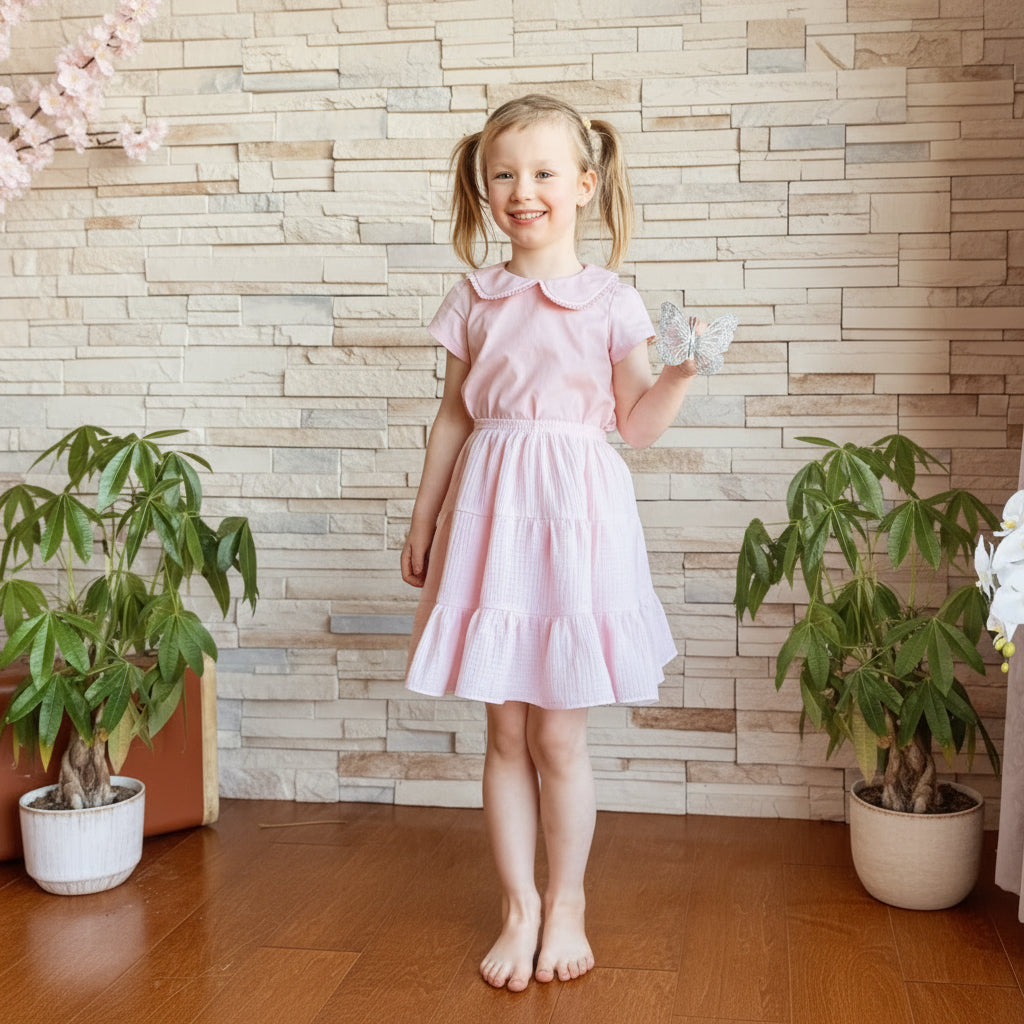 Young girl in a pink dress standing against a stone wall.