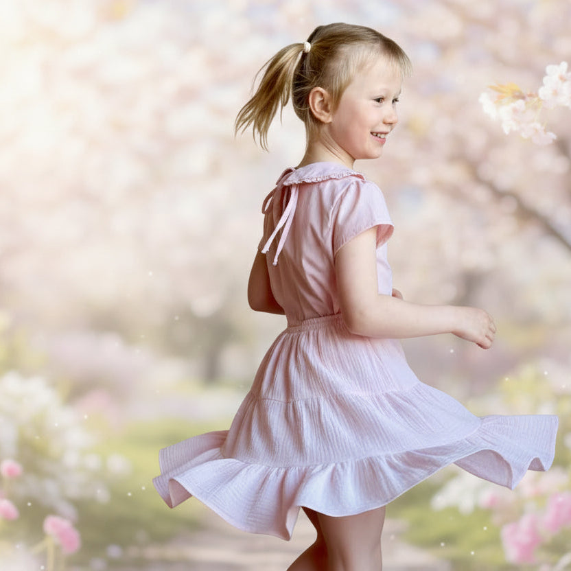 Young girl in a pink dress standing against a stone wall.