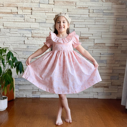 Young girl in a pink dress standing in front of a stone wall.