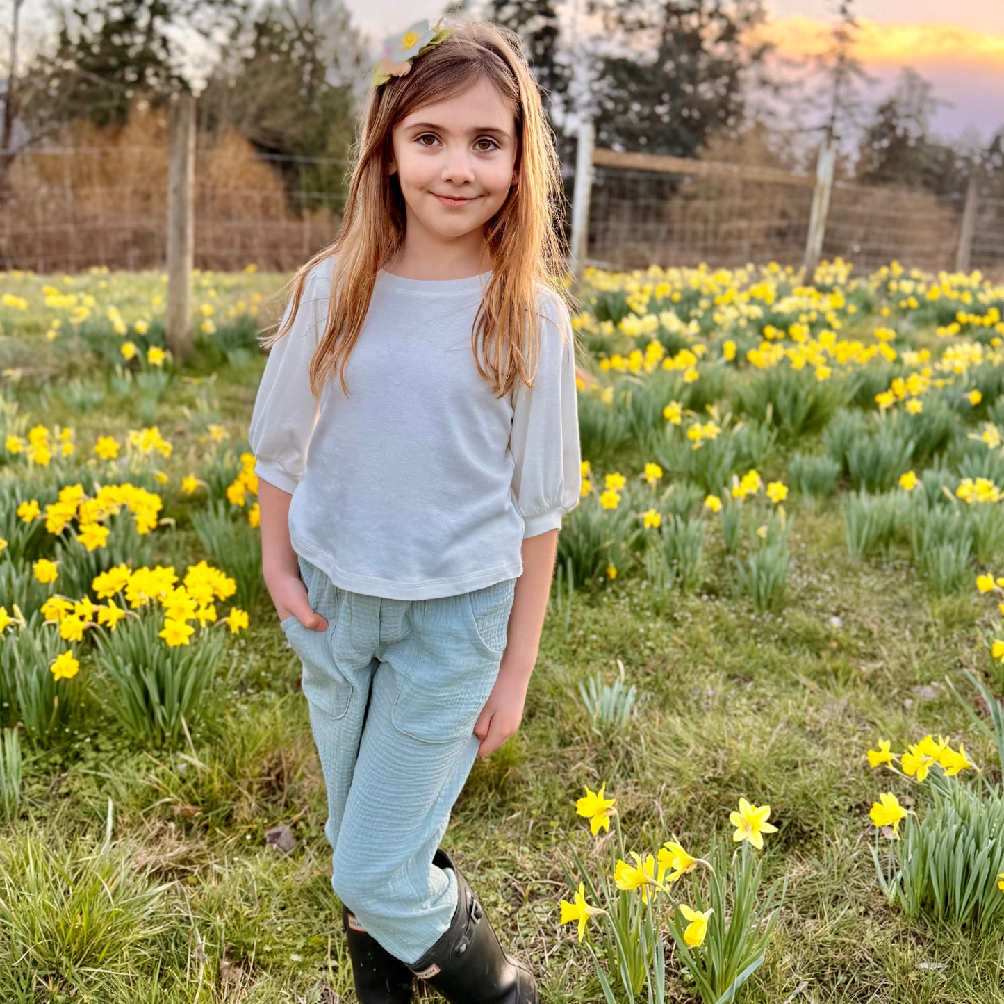 Young girl standing in a field of yellow flowers with a sunset in the background