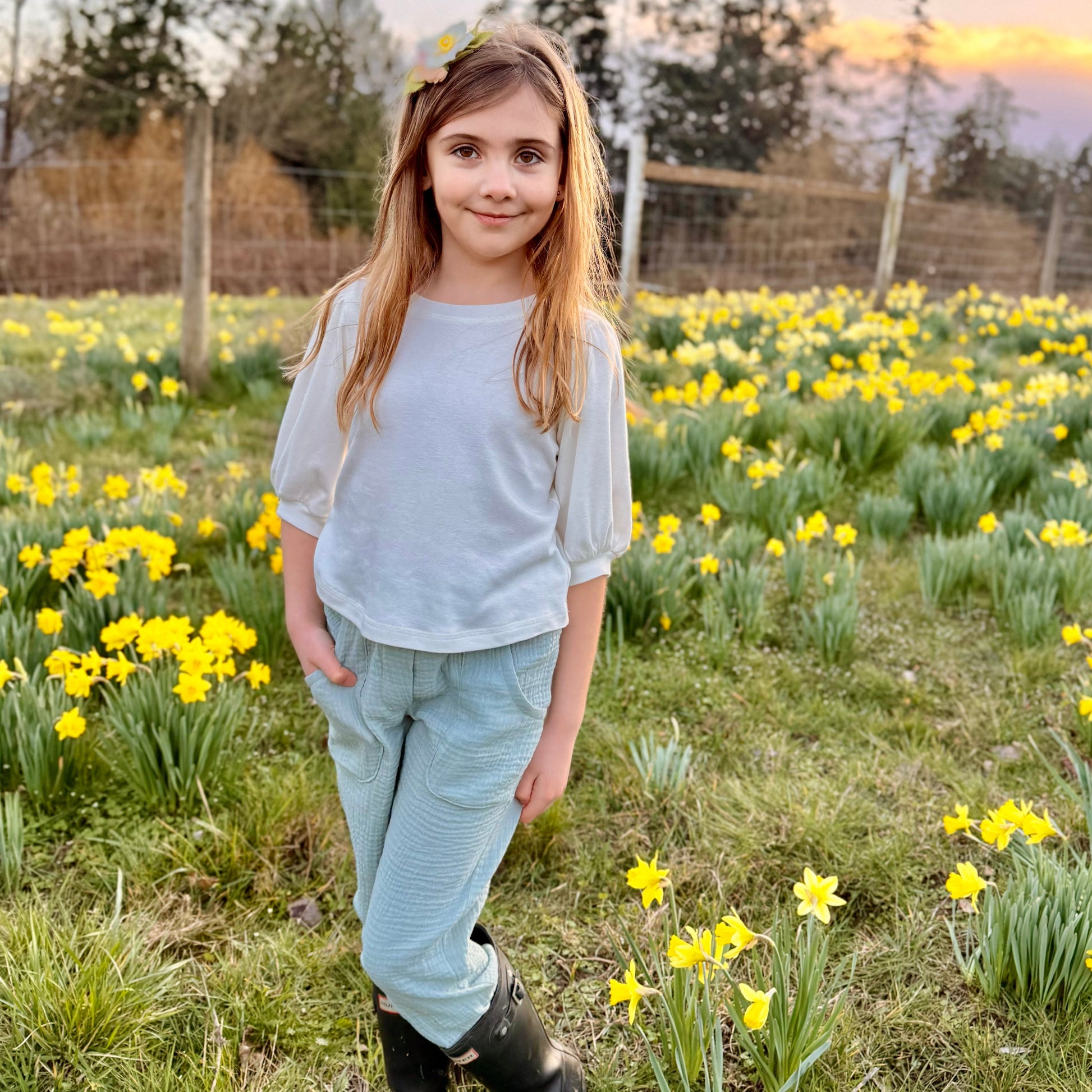 Young girl standing in a field of yellow flowers with a sunset in the background