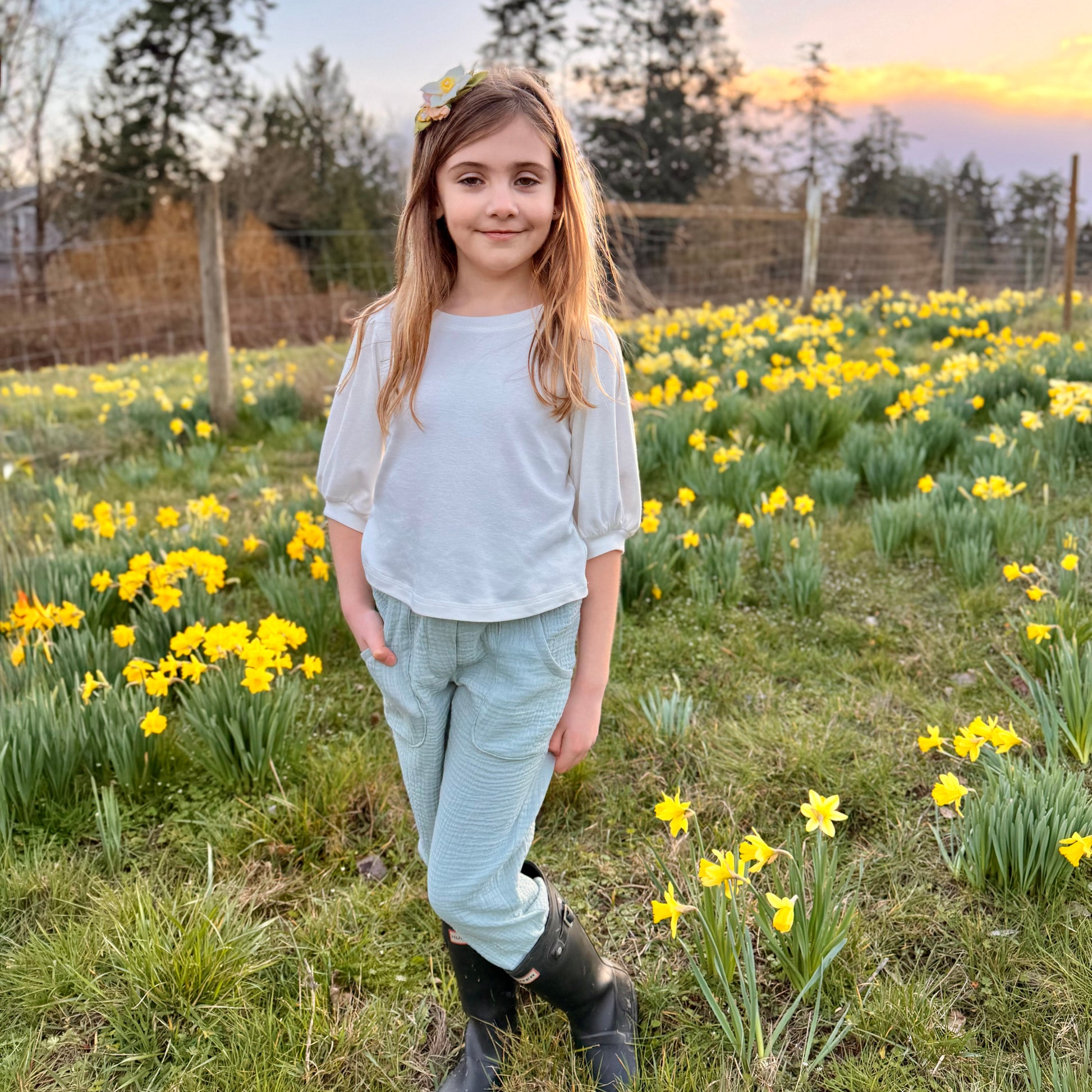 Young girl standing in a field of yellow flowers with a sunset in the background