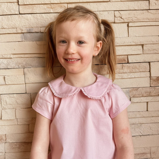 Young girl in a pink dress with a stone wall background