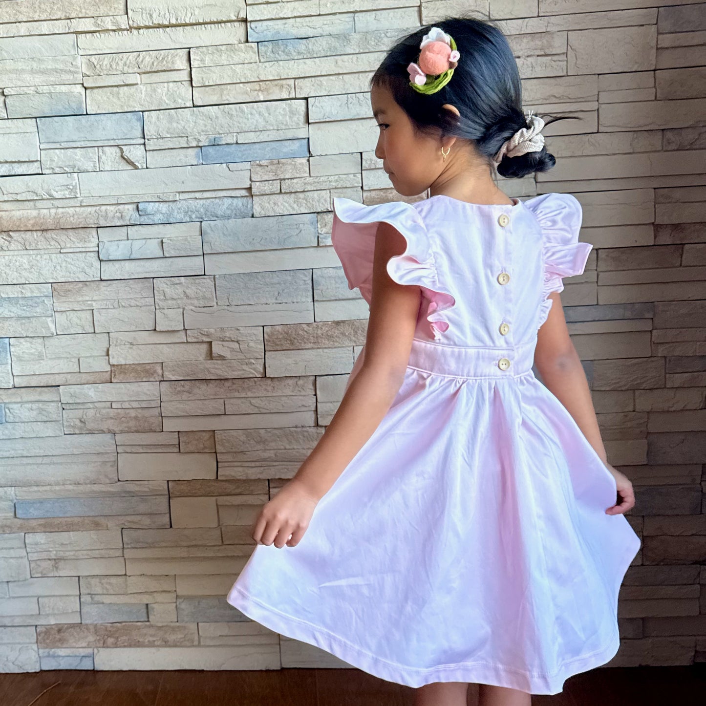 Young girl wearing a white dress with ruffled sleeves against a brick wall.