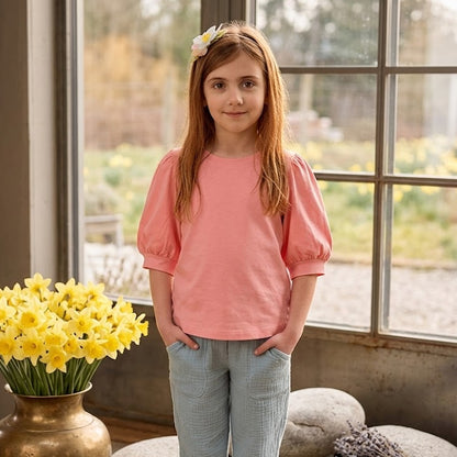 Young girl in a pink shirt standing in a room with yellow flowers and stones.