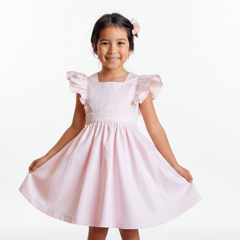 Young girl in a white dress standing against a brick wall.